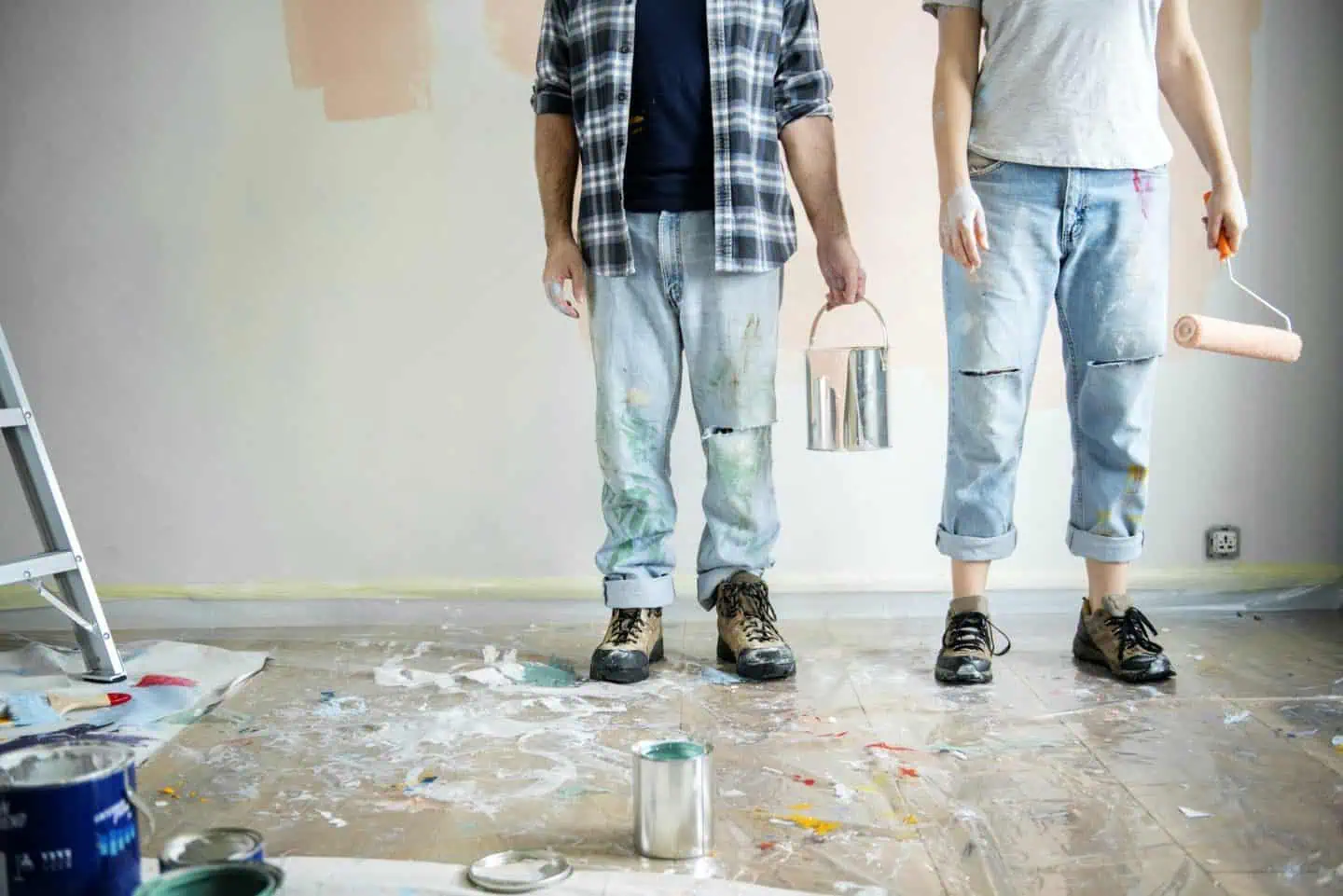 Two painters standing in a room with painting supplies and a partially painted wall.